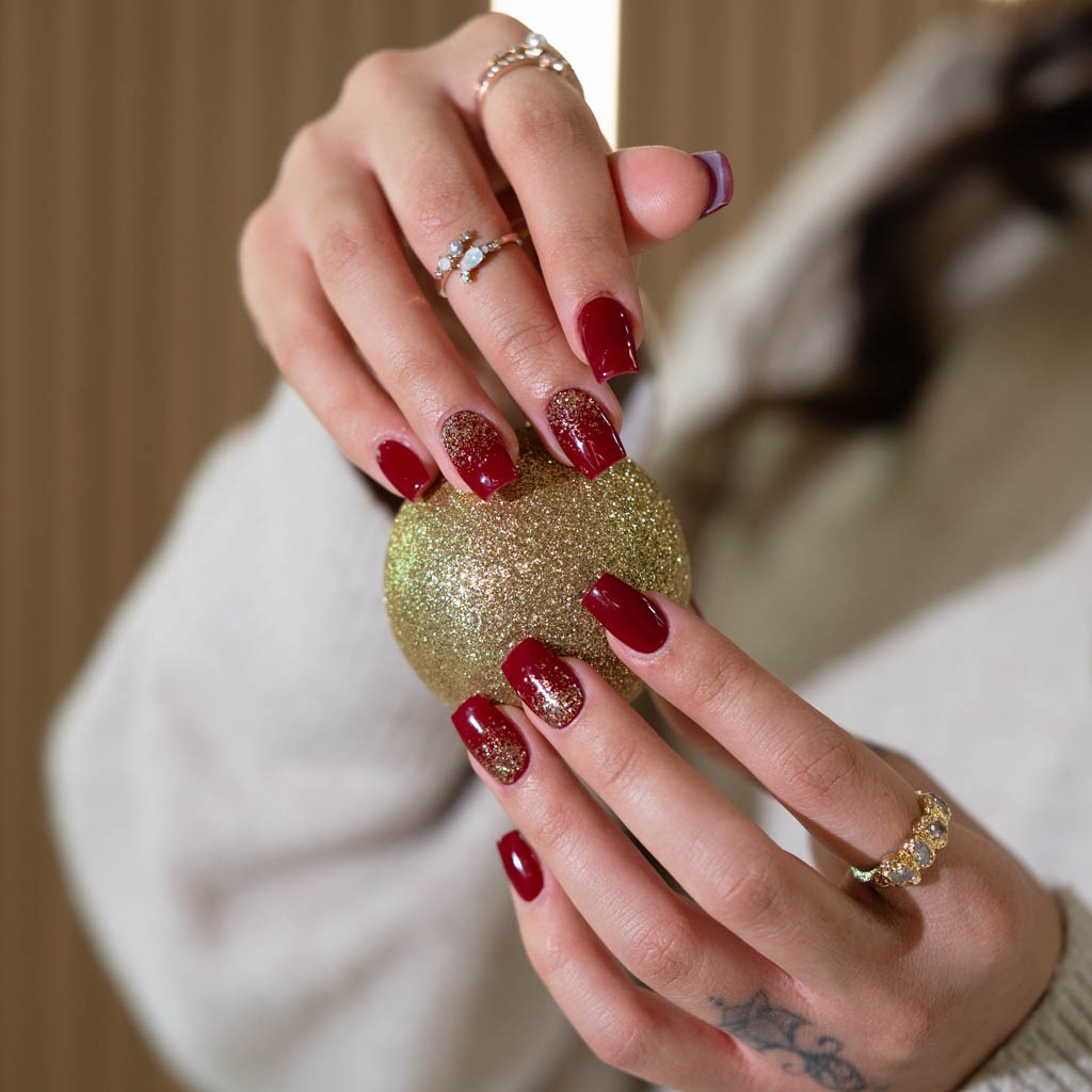 Luxury red gel nails with gold glitter accent at H’ONU featuring glossy finish and elegant manicure detail